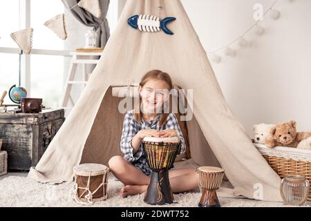 Kleines Mädchen spielt auf traditionellen afrikanischen Djembe Trommeln sitzen in Wigwam zu Hause Stockfoto
