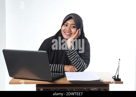 Porträt einer asiatischen Frau in legerer Kleidung in einem Büro. Eine verschleierte Frau mit einem glücklichen Ausdruck arbeiten an einem Computer. Das Konzept eines su Stockfoto