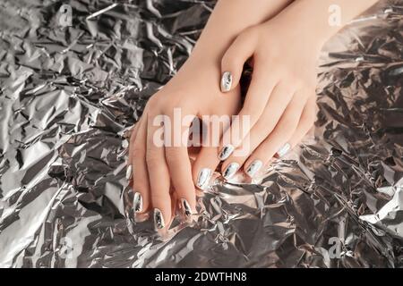 Weibliche Hände mit trendigen silbernen Nagel-Design auf Folie Hintergrund. Festliche Kulisse für Feiertage. Flache Lay-Optik. Stockfoto