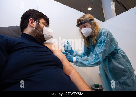 Greven, Deutschland. Dezember 2020. Anja Büscher (r), medizinische Assistentin des Verbandes der gesetzlichen Krankenversicherungsärzte, legt zu Testzwecken eine Spritze auf den Arm von Leon Berisa vom Technischen Hilfswerk (THW) im Impfzentrum des Kreises Steinfurt. Am Flughafen des Impfzentrums startete ein Testlauf mit rund 50 Testpersonen aus THW, DLRG, Malteser, DRK Kreisverband ST und DRK Kreisverband TE. Quelle: Guido Kirchner/dpa/Alamy Live News Stockfoto