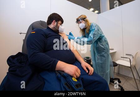 Greven, Deutschland. Dezember 2020. Anja Büscher (r), medizinische Assistentin des Verbandes der gesetzlichen Krankenversicherungsärzte, legt zu Testzwecken eine Spritze auf den Arm von Leon Berisa vom Technischen Hilfswerk (THW) im Impfzentrum des Kreises Steinfurt. Am Flughafen des Impfzentrums startete ein Testlauf mit rund 50 Testpersonen aus THW, DLRG, Malteser, DRK Kreisverband ST und DRK Kreisverband TE. Quelle: Guido Kirchner/dpa/Alamy Live News Stockfoto