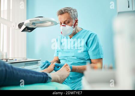 Chiropodisten podiatrist in blauer Uniform und Handschuhe mit medizinischem Werkzeug In der Hand während der Behandlung Verfahren an den Füßen Stockfoto