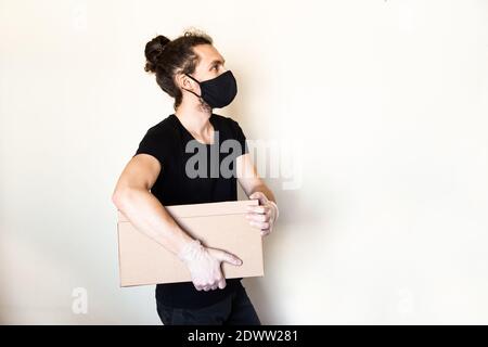 Junger Mann mit Maske und Handschuhen hält eine Schachtel aus. Angestellter des Lieferers. Service während des Coronavirus-Pandemiekonzepts. Stockfoto