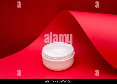 Glas Schönheit Creme auf rot Welle Papier Hintergrund Stockfoto