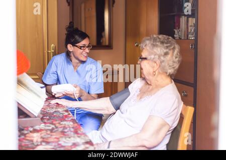 Glückliche ältere Frau, die den Blutdruck von ihrem Betreuer zu Hause nimmt. Pflegekonzept für Senioren. Stockfoto