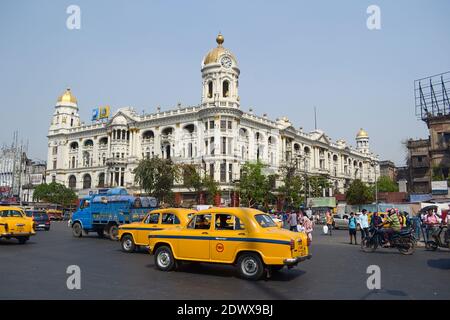 Kolkata, Indien - März 2014: Fahrzeuge und Menschen an der Kreuzung vor dem Metropolitan Building in Esplanade. Historisches Haus mit Uhrenturm Stockfoto