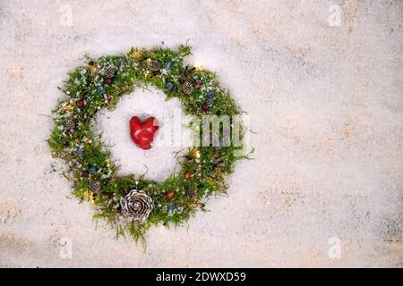 Weihnachtskranz mit grünem Moschus, Beeren, kleinen Kiefern und Lichtern auf einem Schneeteppich. Handgemachte natürliche Dekoration, um Liebe zu Weihnachten zu verbreiten. Stockfoto