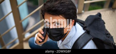 Portrait eines jungen Mannes mit Maske, sitzt er auf der Essstappe und telefoniert. Stockfoto