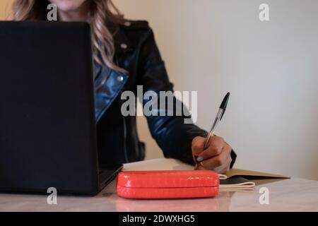 Nahaufnahme einer jungen Frau, die an einem Tisch sitzt. Sie schreibt in ihr Notizbuch Stockfoto