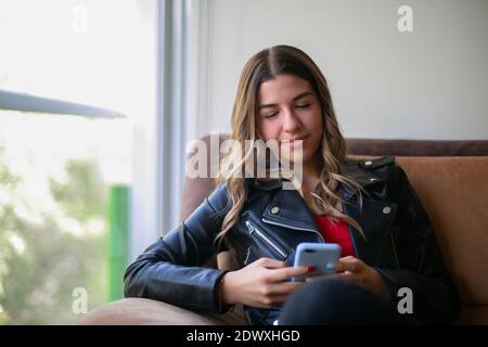 Junge Frau, die in ihrem Sessel sitzt und ihr Telefon hält Stockfoto