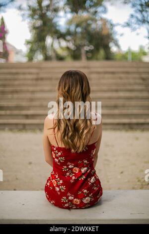 Frau trägt ein rotes Kleid. Sie sitzt auf einer grauen Bank. Vor dem Hotel gibt es einige Treppen Stockfoto