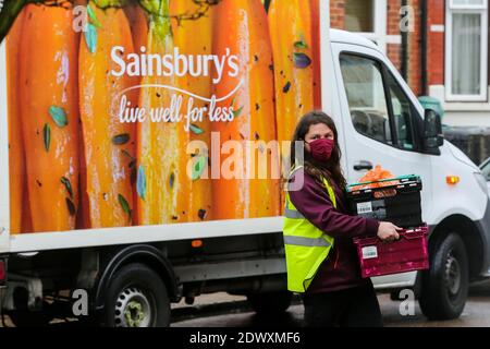 Ein Sainsbury's Deliveryman trägt eine Gesichtsmaske trägt Kisten, während er die Einkäufe an einen Kunden in London liefert. Stockfoto