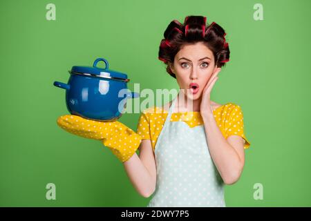 Foto von attraktiven Dame Kochen Lockenwickler Hairdo charmante Hausfrau halten Fertiggericht Gericht Suppe große Pfanne Hand auf Wange tragen pinup gepunktete Schürze Kleid Stockfoto