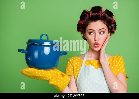 Foto von attraktiven Dame Kochen Lockenwickler Frisur Hausfrau halten bereit Mahlzeit Gericht Suppe große Pfanne Hand auf Wange lecker Meisterwerk Tragen pinup gepunktete Kleid Stockfoto