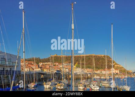 Am Yachthafen in Scarborough. Boote im Hafen mit Geschäften und Cafés Gebäude säumen die Uferpromenade festgemacht, ein Hügel mit einer Wand erhebt sich über Sie Stockfoto