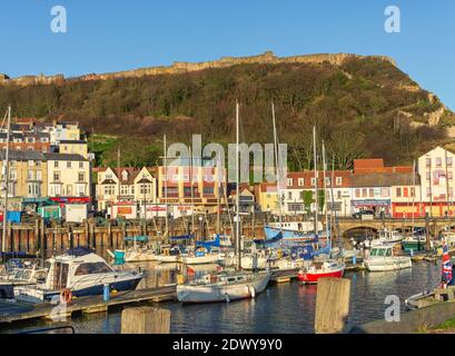 Am Yachthafen in Scarborough. Boote im Hafen mit Geschäften und Cafés Gebäude säumen die Uferpromenade festgemacht, ein Hügel mit einer Wand erhebt sich über Sie Stockfoto