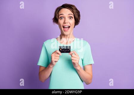 Foto von beeindruckt süße junge Frau gekleidet lässig türkis Kleidung Halten Kreditkarte isoliert violetten Hintergrund Stockfoto