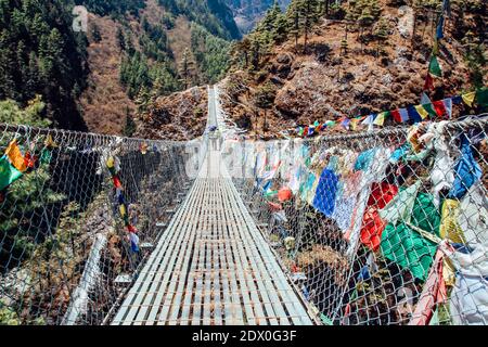 Nepalischer Porter trägt schwere Last auf dem Rücken und geht die Brücke entlang zum Everest-Basislager. Himalaya. Nepal. Stockfoto