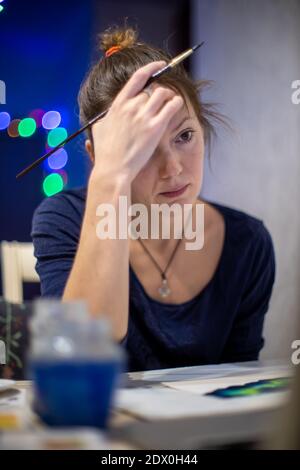 Porträt einer kreativen jungen Frau, die in einer Künstlerwerkstatt an einem Tisch sitzt und pensiver nach Inspiration sucht Stockfoto