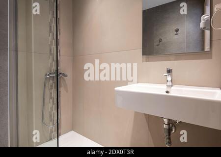 Modernes Interieur eines kleinen Toilettenzimmers mit Glasdusche und weißem rechteckigem Waschbecken, strukturiertem Mosaik und massiven Steinfliesen Stockfoto