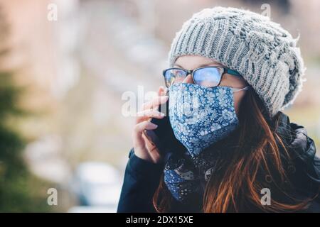 Telefonieren Frau trägt handgemachte Tuch Gesichtsmaske. Es wird empfohlen, nichtmedizinische Gesichtsmasken zu tragen, um die Ausbreitung des Corona-Virus zu verlangsamen. Stockfoto