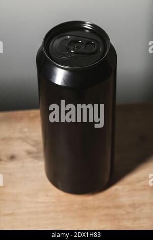 Geschlossene glänzende schwarze Aluminium-Dose steht auf einem Holztisch, Standard-Softdrink-Verpackung. Vertikales Foto Stockfoto