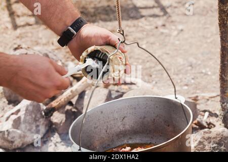 Hinzufügen eines Rindfleischeintopf zu einer Suppe in einem Kessel, Camping Mahlzeit auf offenem Feuer vorbereiten Stockfoto