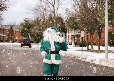 Der Weihnachtsmann tritt im Haus in Heiligabend auf das Tragen ein Eine Tüte mit Kindern, die Geschenke machen, die die Straße entlang gehen Bei Schneefall Stockfoto