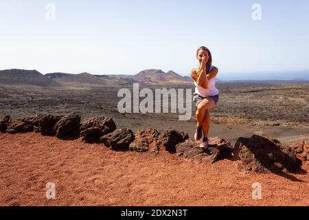 Frau mittleren Alters, die Adler-Yoga macht Pose auf Felsen im Timanfaya National Park. Flexible Yogi in garudasana an sonnigen Tag auf Lanzarote Wahrzeichen Stockfoto