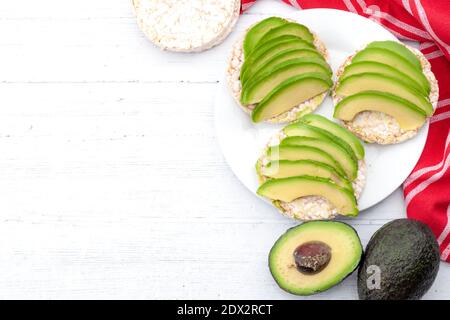 Omega-3-reiche Lebensmittel, vegane Ernährung und nahrhaftes gesundes Lebensmittelkonzept mit rohen Avocado-Früchten und Scheiben auf Reiskuchen Sandwiches auf rustikalem Weißholz-Bac Stockfoto