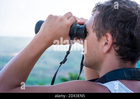 Junger Mann, der aus der Höhe durch das Fernglas schaut Stockfoto