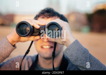 Glücklicher junger Mann, der während des Sonnenuntergangs durch das Fernglas schaut Stockfoto