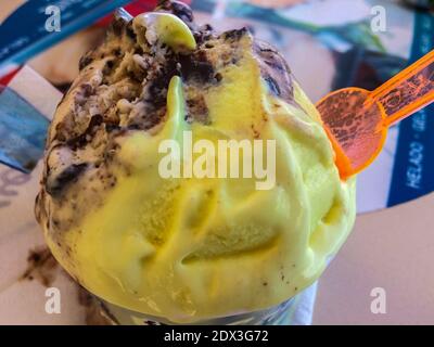Schmelzendes Eis mit Zitronen- und Schokoladengeschmack aus der Nähe und Kunststoff Orangefarbener Löffel Stockfoto