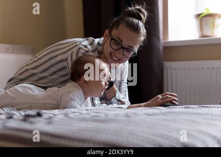 Kindheit, Mutterschaft, Familienkonzepte - erfolgreiche lächelnde reiche Geschäftsfrau Lady Mutter sitzen auf dem Bett mit Kleinkind Kind Baby sprechen am Telefon arbeiten Stockfoto