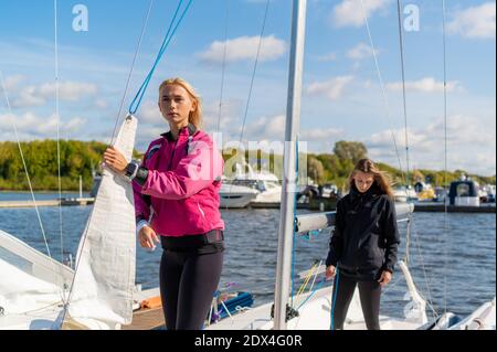 Zwei junge blonde Mädchen an einem sonnigen Sommertag auf einem Segelboot bereiten sich auf einen Flussausflug vor. Stockfoto