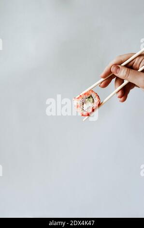 Hand einer jungen Frau, die Sushi-Sticks und eine Philadelphia-Rolle hält. Hochwertige Fotos Stockfoto