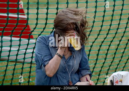 Frau trinkt bei einem Outdoor-Event ein Pint Bier, während starker Wind ihr Haar über das Gesicht bläst. Windgepeitschte Person, die das Wetter nicht verderben lässt Stockfoto