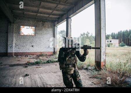 Soldat in voller US MARSOC bewaffnet mit Sturmgewehr durch das verlassene Gebäude laufen. Militärischer Zusammenstoß. Stockfoto