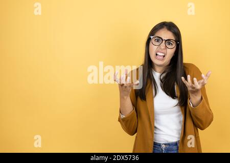 Junge schöne Frau trägt einen Blazer über isolierten gelben Hintergrund verrückt und verrückt schreien und schreien mit aggressivem Ausdruck und Arme angehoben. Stockfoto