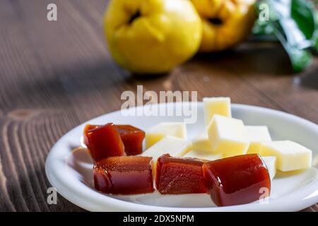 Scheiben hausgemachte Quitten-Marmelade und Käse auf dem weißen Teller, frische reife Quitten-Früchte auf dem Holztisch. Typisch spanisches Dessert. Stockfoto