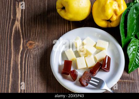 Scheiben hausgemachte Quitten-Marmelade und Käse auf dem weißen Teller, frische reife Quitten-Früchte auf dem Holztisch. Typisch spanisches Dessert. Stockfoto