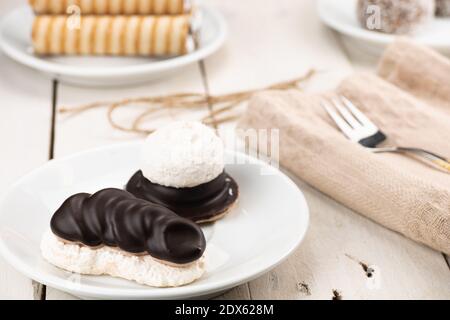 Kokosnusskuchen mit Kakaocreme-Füllung und Schokoladenüberzug. Serviert auf einem Holztisch und einer goldenen Gabel auf einem weißen Teller. Hochzeitsdessert. Hausgemachtes Backen Stockfoto