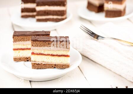 Hochzeitstorte mit Schokoladenüberzug, Kakao- und Keksteig, Schokoladencreme und Erdbeermarmelade. Dessert ist auf weißem Holztisch im Retro-Stil. Stockfoto
