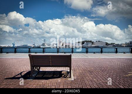 Eine Parkbank im Verny Park in Yokosuka, Japan mit US-Schiffen und japanischen U-Booten legte im Hintergrund an der US Navy Base gegenüber dem Hafen an. Stockfoto