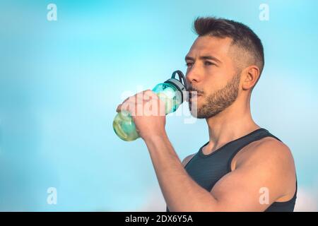 Junge Fitness muskulösen Mann trinken Detox Zitronenwasser aus wiederverwendbaren Flasche während eines Trainings. Trinken während des Trainings. Stockfoto