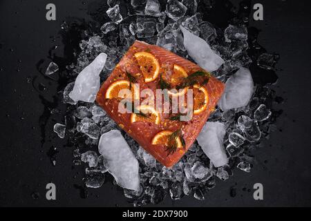Rohes Lachsfilet mit Orangenscheiben auf Eisstücken Auf schwarzem Hintergrund Stockfoto