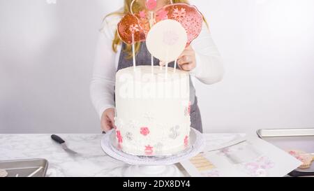 Einfügen von großen Lutscher mit Schneeflocken in den hohen Weiße, runde Kuchen als Dekoration. Stockfoto