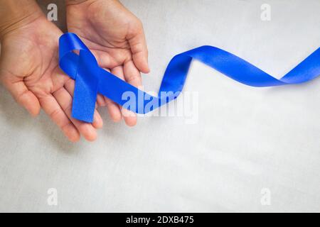 Hände mit tiefblauem Band auf weißem Stoff mit Kopierraum. Darmkrebs Bewusstsein, Colon Krebs der älteren Person und Welt Diabetes Tag, Chil Stockfoto