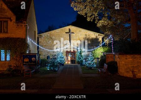 Weihnachtsbäume und Dekorationen in der Nacht vor der vereinigten reformierten Kirche am Broadway. Cotswolds, Gloucestershire, England Stockfoto