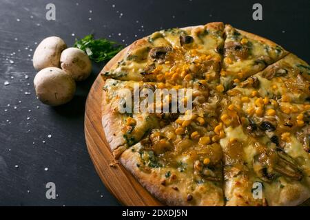 Draufsicht köstliche Pizza mit Zutaten Mozzarella Käse, Mais karamellisierte Zwiebeln Pilze mit einer Basis von weißer Sauce auf einem schwarzen rustikalen Holz Bac Stockfoto